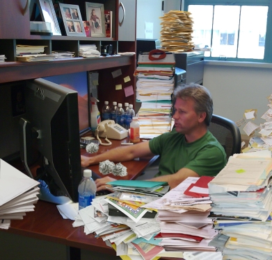 Ralph behind desk with lots of paperwork